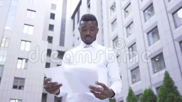 一个英俊的非洲裔美国人穿着白色衬衫站在城市街道上阅读文件男性视频的预览图