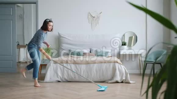 有创意的女孩在家里的卧室里用拖把唱歌跳舞洗地板视频的预览图