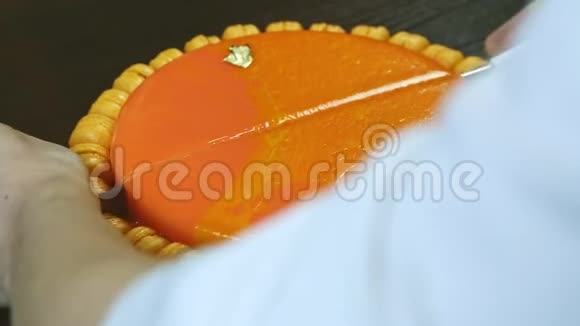 双手用大刀切成两半用橙色镜面釉切成圆形芝士蛋糕视频的预览图