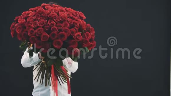 年轻人站着捧着一大束红玫瑰眼睛望着它肩膀上走着视频的预览图