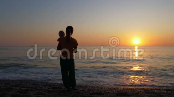 母亲抱着婴儿看着海边或海边的日落视频的预览图