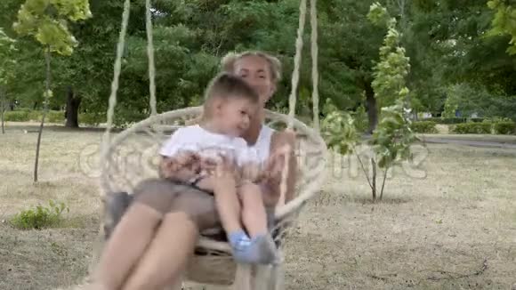 年轻的妈妈和宝宝在公园里荡秋千玩孩子坐在妈妈腿上他们微笑着视频的预览图