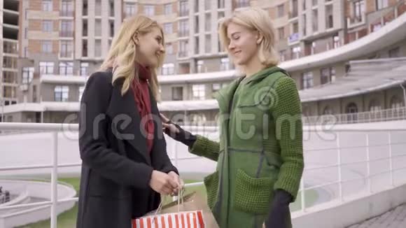 两个漂亮的金发女朋友站在街上互相展示购物袋两个时装女秀视频的预览图