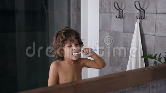 有棕色卷发的英俊小男孩在睡前或睡后刷牙时使用牙膏和牙刷视频的预览图