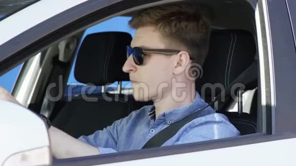 穿着休闲服装和太阳镜的布鲁内特男子正在他的车里听蓝色屏幕背景的音乐他在跳舞视频的预览图