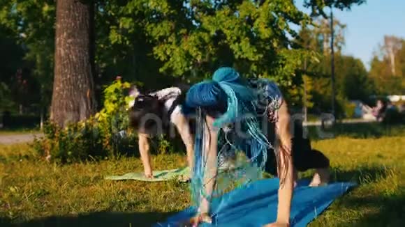 两个年轻的运动女性在公园里做瑜伽运动一个女人有长长的蓝色恐惧症视频的预览图