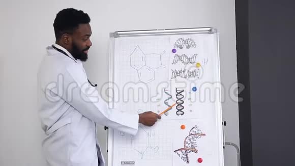 迷人的年轻留胡子的深色皮肤医生讲课并解释海报上的化合物视频的预览图