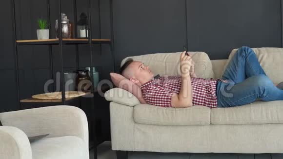 一个人躺在沙发上使用智能手机视频的预览图