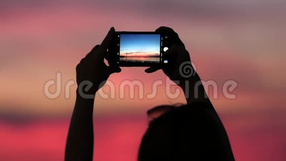 女人在日落时用智能手机拍照视频的预览图