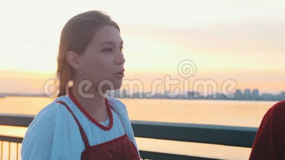日落时分穿着俄罗斯民族服饰的人们站在海滨唱着一首歌现代建筑在视频的预览图