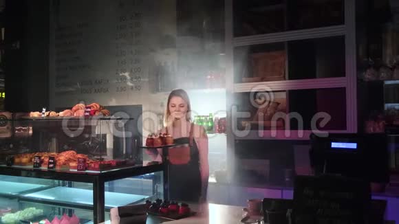 漂亮的女售货员拿着一盘新鲜蛋糕站在糕点店柜台后面视频的预览图