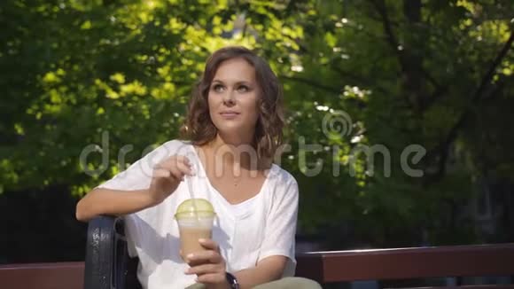 快乐的中年妇女喝着拿铁和冰坐在市中心的长凳上视频的预览图