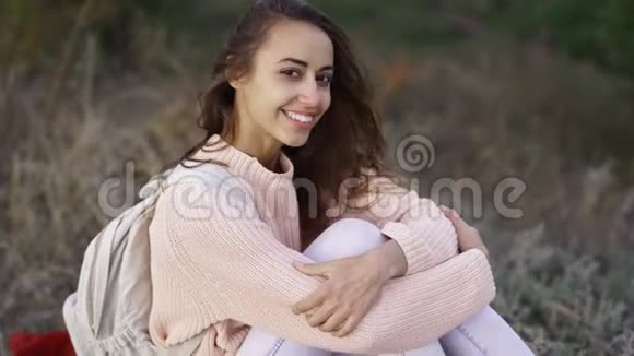 一个穿着针织粉色毛衣的漂亮女孩的特写小背包坐在Autamn森林的毯子上视频的预览图