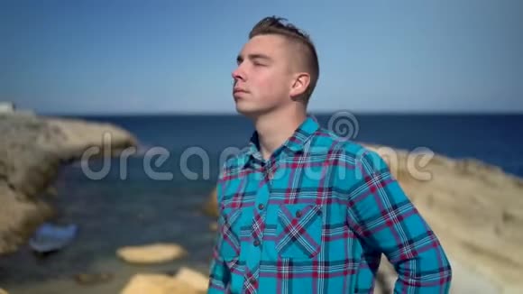 一个年轻人站在大海的背景上一个穿蓝色衬衫的人戴太阳镜探索周围的自然视频的预览图