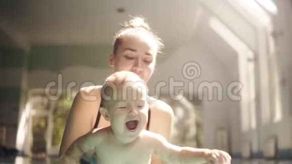 快乐的年轻妈妈和可爱的可爱宝宝在游泳池游泳微笑的妈妈和小孩男孩玩得开心视频的预览图