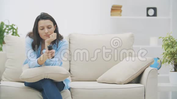 慢点漂亮的女人看电视无聊坐在家里的沙发上突然她听到了惊人的消息视频的预览图