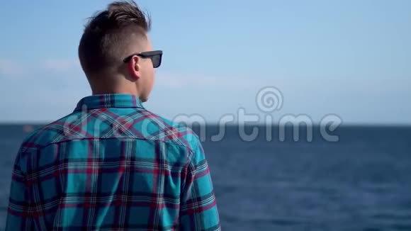 一个年轻人看着大海穿蓝色衬衫的人钦佩大自然一个人背对着摄像机站着视频的预览图