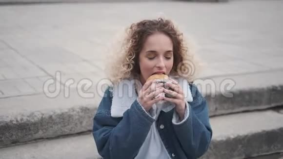 坐在台阶上吃汉堡的年轻女人视频的预览图