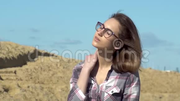 一个年轻的女人坐在大海背景上的石头上风吹在女孩的头发上阳光照在脸上视频的预览图
