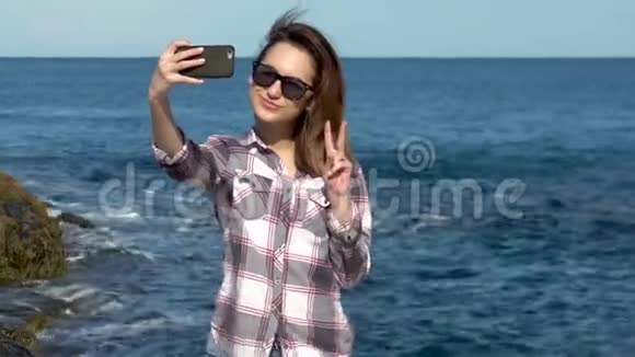 年轻女子在大海背景下的智能手机上自拍女人在假期拍照阳光明媚的蓝海视频的预览图