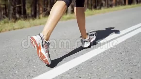 美丽的白种人女运动员在松林的柏油路上度过了阳光明媚的夏日腿的视图慢动作视频的预览图