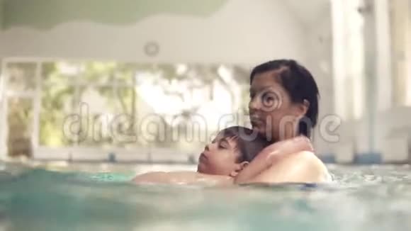 小男孩和他妈妈一起在游泳池里游泳她把他从后面抱起来教他如何游泳视频的预览图