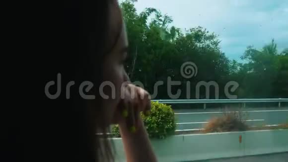 一个年轻的女人坐在公共汽车里看着窗户看着路和车视频的预览图
