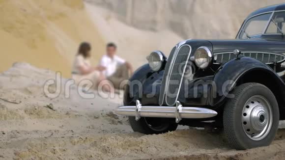 日落时的沙漠前景是一辆黑色复古车在背景中一男一女坐在视频的预览图