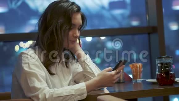 女孩独自坐在咖啡馆里使用智能手机灯光背景下一个少年在咖啡馆的画像视频的预览图