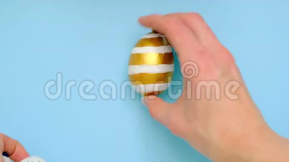 雌性手在一张蓝色的桌子上产卵5个复活节彩蛋鸡蛋时髦的彩色经典蓝色白色和金色复活节快乐视频的预览图