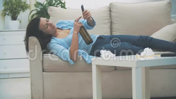 慢点一个瘦小的黑发女人正在手机上输入一条信息手里拿着一瓶空啤酒视频的预览图