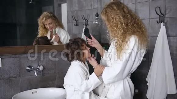 可爱的女人穿着白色浴袍梳着卷发她的小儿子在家里的浴室里每天的卫生快乐视频的预览图