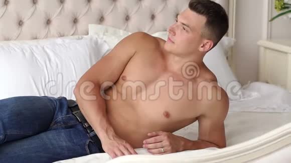 早上穿牛仔裤没有衬衫的漂亮运动男人躺在床上视频的预览图