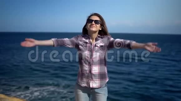 年轻的女人在大海的背景下举起双手阳光明媚的天气里戴太阳镜的女孩女孩得到视频的预览图