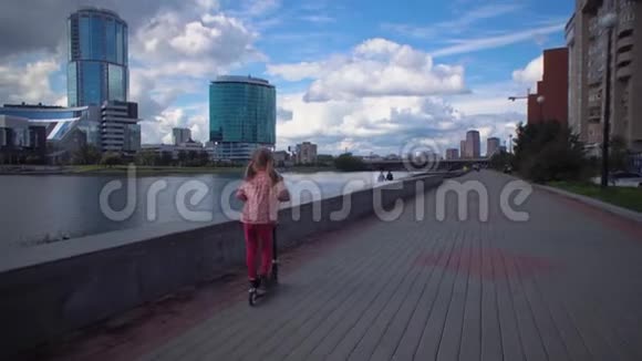 小女孩骑着两轮摩托车沿着市中心的河边视频的预览图