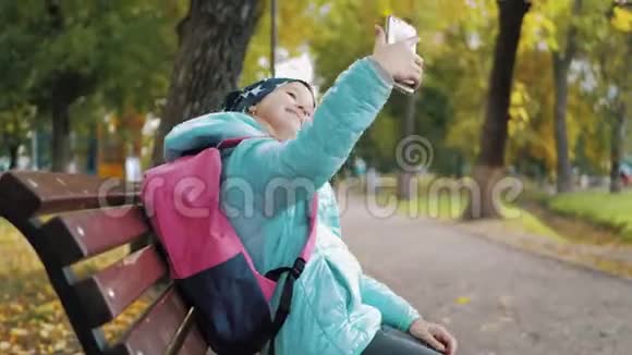 金秋时节一位美丽的少女坐在公园的长椅上用手机自拍视频的预览图
