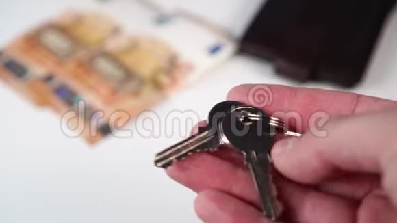 一个男人手里拿着一带着欧元钞票和一个白色背景钱包的闪亮的新公寓钥匙视频的预览图