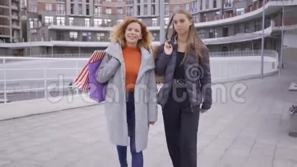 两个快乐的白种人女孩拿着购物袋走路两位时尚女性聊天分享前进的新闻视频的预览图