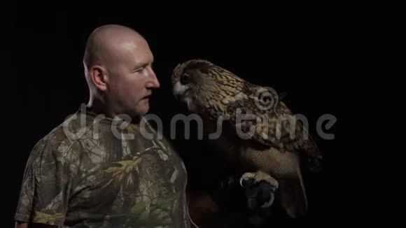 一只成年猫头鹰坐在驯兽师的手上摸着他的脸视频的预览图