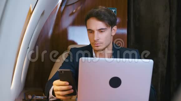 年轻的商人在笔记本电脑上工作在私人飞机上使用智能手机成功的生意视频的预览图