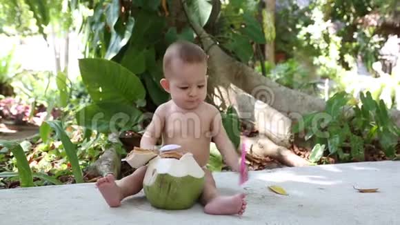 婴儿正坐在街上手里拿着新鲜的绿色椰子找一根吸管喝牛奶视频的预览图