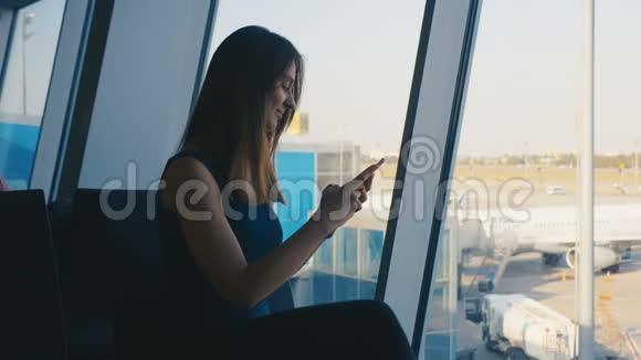 年轻女性旅客在机场候机楼使用智能手机视频的预览图