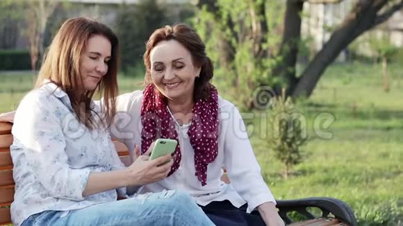 两个有魅力的快乐的中年女性女友使用智能手机视频的预览图