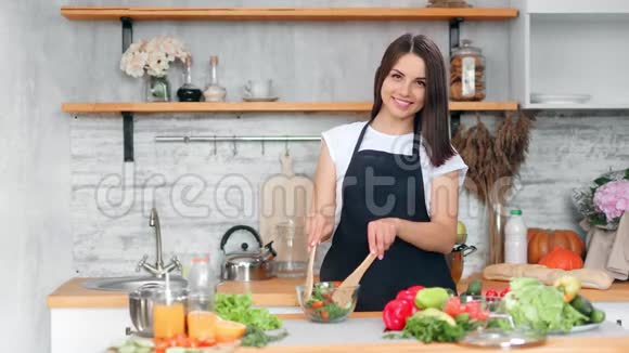 可爱的年轻纯素女人在厨房摆姿势的碗里混合新鲜开胃的沙拉视频的预览图