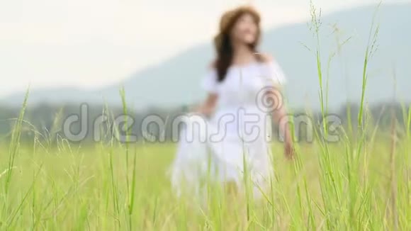 穿着白色衣服的亚洲女人正漫步在辽阔的草原上用手触摸绿草的顶端在草地上散步的女孩视频的预览图