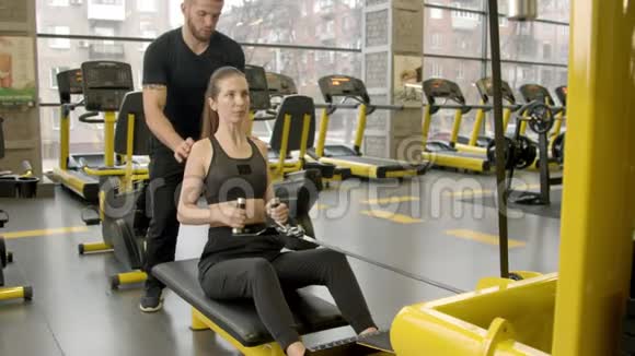 有教练的年轻女子用赛艇机在健身房锻炼视频的预览图