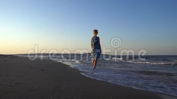 穿着裙子的苗条甜美女人光着脚在沙滩上散步背景是海浪和大海视频的预览图