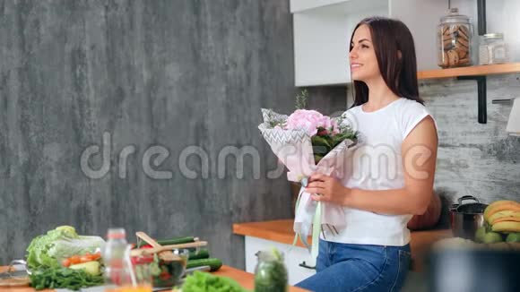 可爱的休闲少女在厨房里嗅着粉红色温柔的花束视频的预览图