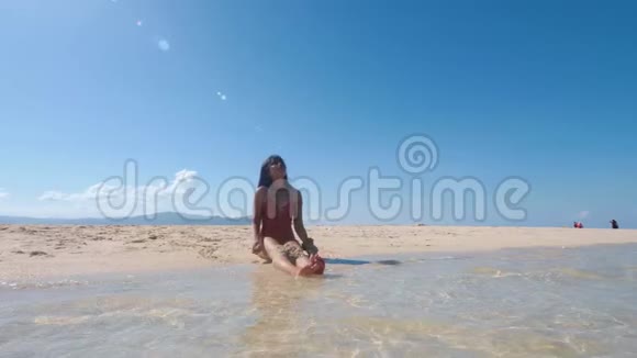 一个快乐的女孩坐在海滨把细沙抛在空中笑着视频的预览图