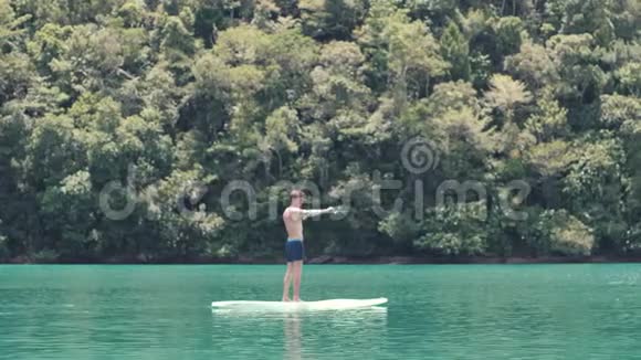站起来的桨板上的年轻人漂浮在一个绿色的泻湖里做热身视频的预览图